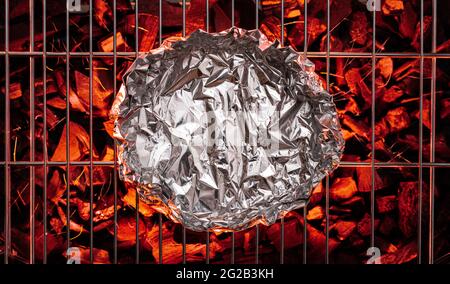 Aluminum foil on  grate over hot pieces of coals. Top view. Stock Photo