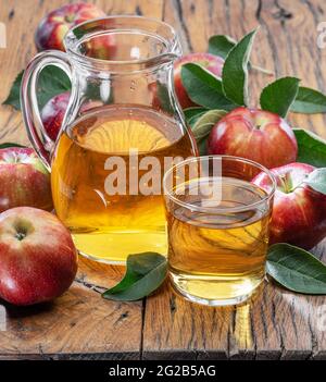 Glass and carafe of fresh apple juice and organic apples on dark old wooden table. Stock Photo