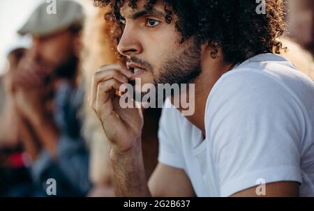 Man looking worried while watching a match at stadium. Man biting nails while watching a live soccer game from stands. Stock Photo