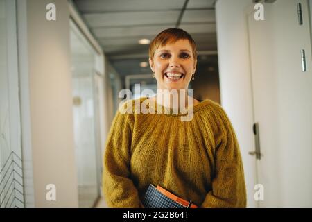 Happy woman standing in office corridor. Woman executive in office smiling and standing at office corridor. Stock Photo