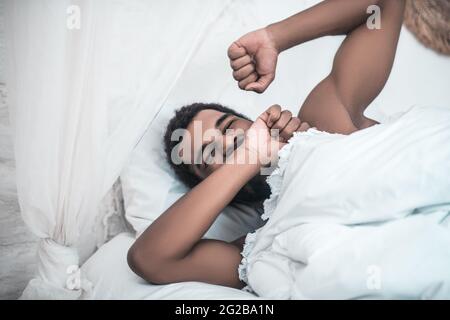 Sleepy yawning darkskinned man in white bed Stock Photo
