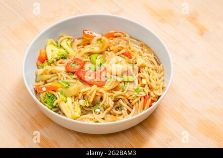 Golden coloured spicy sea food noodles with shrimp, broccoli, chilli pepper in a plate on wooden table Stock Photo