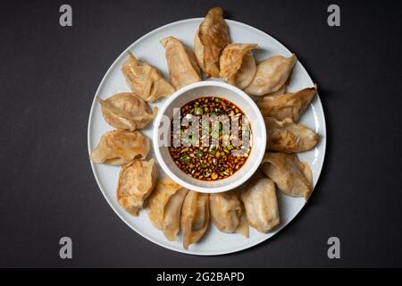 Fried gyoza style dumplings in a plate with spicy soy sauce on black background. Take away asian food. Stock Photo