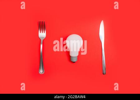 Romantic valentines day dinner idea concept. Light bulb on plate and silver wear on red background. Stock Photo
