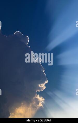 Sunlight rays streak beams came from the big cloud in the dark blue sky. Stock Photo