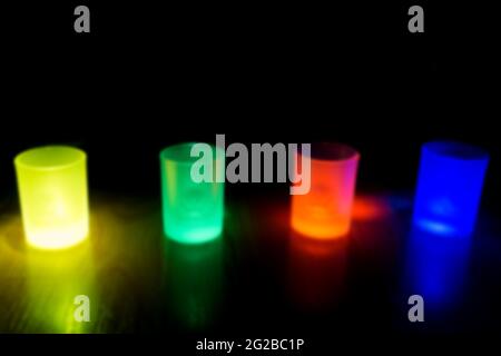 Four shot glasses illuminated in different colors green, yellow, blue and red Stock Photo