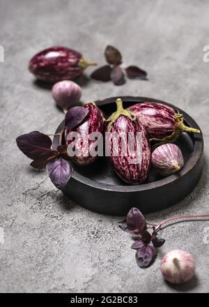 Organic raw purple mini eggplants with garlic and basil on grey stone background Stock Photo