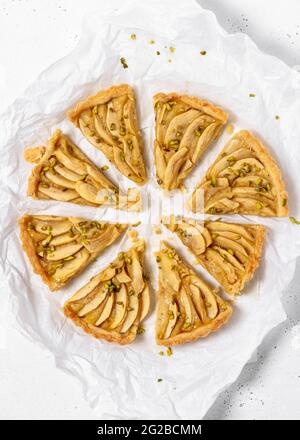 Whole fresh homemade apple pie in many pieces on a white baking paper sheet. Flat Lay. Stock Photo