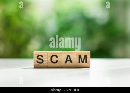 Word scam message sign of wooden cubes on a light table against a background of green leaves in soft focus Stock Photo