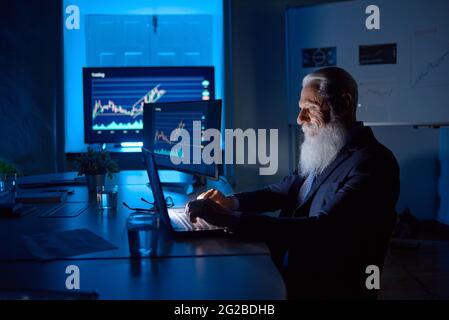 Senior employee typing on laptop in dark office Stock Photo