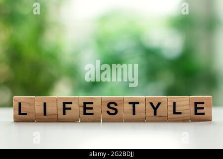 Word lifestyle message sign of wooden cubes on a light table against a background of green leaves in soft focus Stock Photo