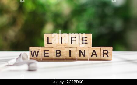 The Word life webinar message wooden letters on a white table against a background of green vegetation, next to white headphones. Business concept, on Stock Photo