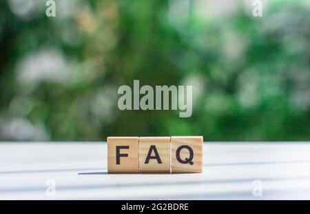 Word  FAQ message sign of wooden cubes on a light table against a background of green leaves in soft focus Frequently asked question concept Stock Photo