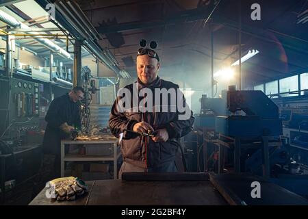 Handyman preparing his autogenous welding tool for work while his colleague can be noticed in the back working on his grinding task. Stock Photo