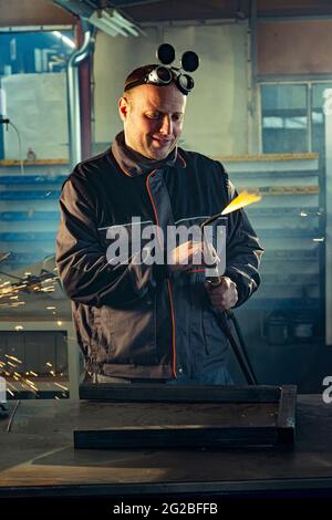 Handyman preparing his autogenous welding tool for work while his colleague can be noticed in the back working on his grinding task. Stock Photo