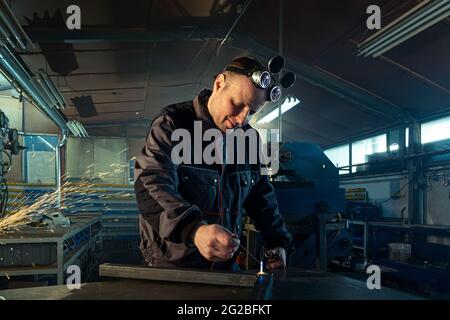 Welder working with autogenous welding tool in workshop while his colleague can be noticed in the back grinding. Stock Photo