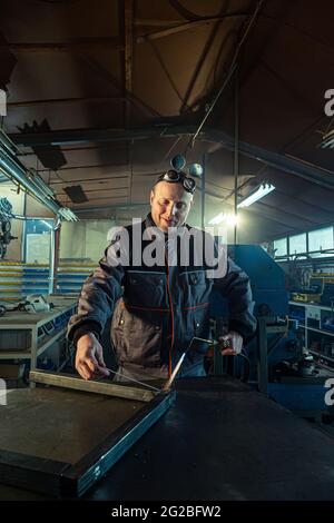 Welder working with autogenous welding tool in workshop while his colleague can be noticed in the back grinding. Stock Photo