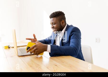 Millennial African American businessman sit at office desk using laptop look at screen read e-mails, hold online meeting, freelancer do remote job Stock Photo