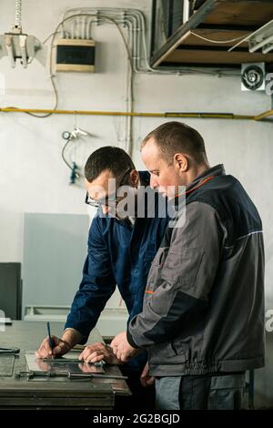 A tinsmith and his fellow colleague engineer are working together on a work task in their workshop. Stock Photo