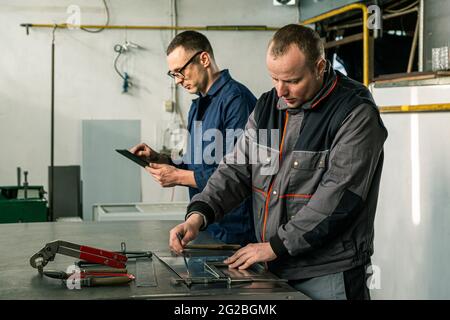 A tinsmith and his fellow colleague engineer are working together on a work task in their workshop. Stock Photo