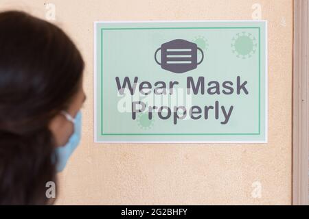 Shoulder Shot of Young girl Student adjusting mask by seeing wear mask properly notice on classroom wall before entering class to protect from Stock Photo