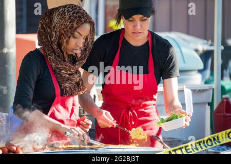 Scenes from Taste of Little Italy festival. Two young muslim women packing fast food in a container at a food stall. The women are in black and red wi Stock Photo