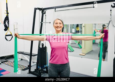 Adult woman doing exercises with resistance bands for recovery of her hands and shoulders after trauma at a rehab clinic Stock Photo