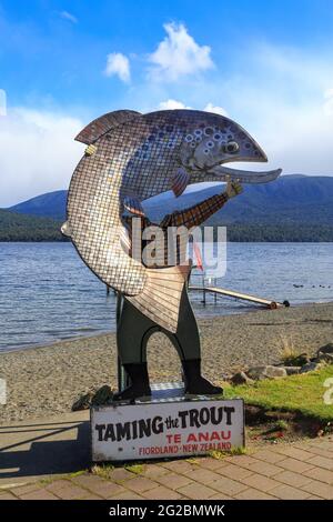 A 'Taming the Trout' photo cutout on the shore of Lake Te Anau, New Zealand, depicting a fisherman holding a giant fish Stock Photo