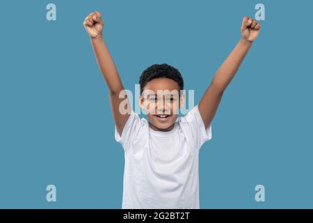 Dark skinned friendly boy with fists raised victoriously Stock Photo