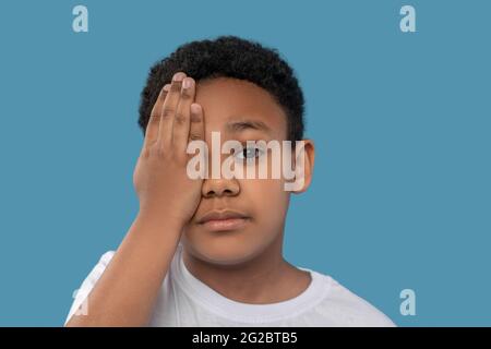 Boy covering one eye with hand Stock Photo - Alamy