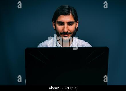Long Haired Brown Hispanic San with Beard Looking Concentrated at his Black Laptop Isolated on Gray Stock Photo