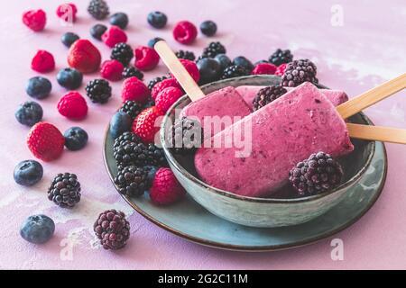 Homemade mixed berry yogurt ice popsicles in a bowl on pink background Stock Photo
