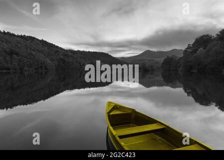 Yellow boat at the lake. Sunset at Chambon lake in Auvergne Volcanic Regional Nature Park, France. Black white yellow vintage toned photo. Retro trave Stock Photo