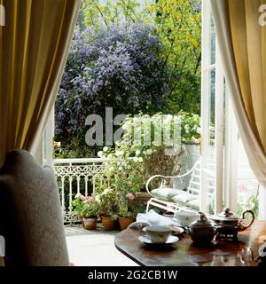 Tea set on table by flower pots on balcony Stock Photo
