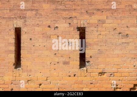 A loophole in an old stone wall. The fortification stone wall of an ancient castle with loopholes. Bullet and cannonball marks on the wall. Textured b Stock Photo