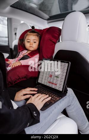Baby girl sitting in car seat while mother using laptop Stock Photo