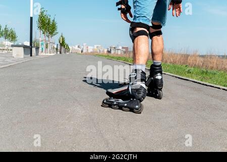 Male legs in roller skates and protective equipment close up riding on the asphalt road in summer, roller-blading, outdoor activity, healthy active li Stock Photo