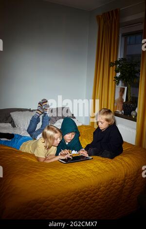 Boys using digital tablet on bed Stock Photo