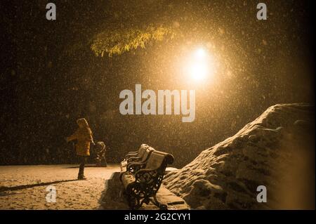 Person walking and enjoying the weather on a snow-covered road on a stormy night Stock Photo