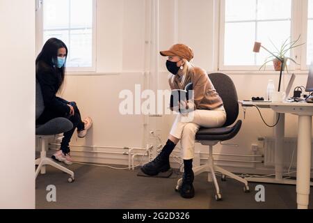 Women in face masks talking in office Stock Photo