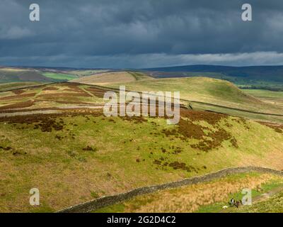 Scenic rural landscape & dark rain clouds (hilly area, rolling sunlit hills, people walking pet dog) - view to Wharfedale, Yorkshire Dales England, UK Stock Photo