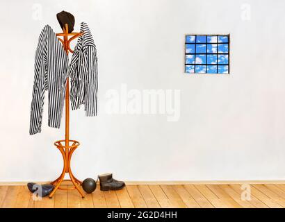 The striped prisoners costume hangs on the coat hook in an empty cell with windows with bars. Stock Photo