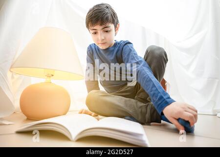 happy caucasian child little boy reading a magic book in a tent at home Stock Photo