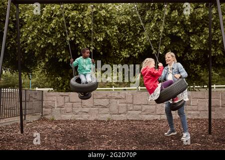 Mother pushing daughter on tire swing Stock Photo