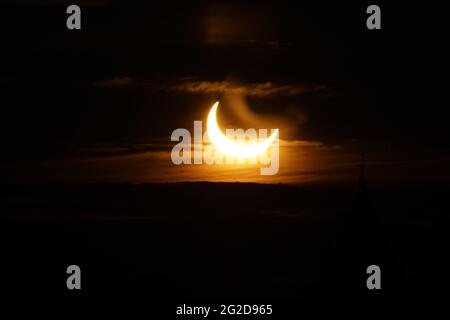 Ottawa, Canada. June 10, 2021: A partial solar eclipse is seen over Parliament Hill in Ottawa, Canada - Thursday, June 10, 2021. The annular or 'ring of fire' solar eclipse is only visible to some people in Greenland, Northern Russia, and Canada. Here, the sun is seen at its maximum eclipse point, less than 3 degrees above the horizon in Ottawa. Credit: George Ross/Alamy Live News Stock Photo