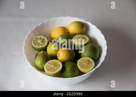 Green limes and yellow lemons inside the white bowl, whole and sliced lemon, citrus Stock Photo