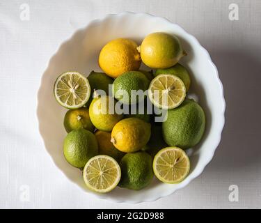 Green limes and yellow lemons inside the white bowl, whole and sliced lemon, citrus Stock Photo