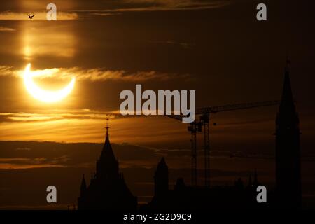 Ottawa, Canada. June 10, 2021: A partial solar eclipse is seen over Parliament Hill in Ottawa, Canada - Thursday, June 10, 2021. The annular or 'ring of fire' solar eclipse is only visible to some people in Greenland, Northern Russia, and Canada. Here, the sun is seen just past the maximum eclipse point only three degrees above the horizon, over the Parliament buildings. Credit: George Ross/Alamy Live News Stock Photo