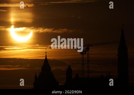 Ottawa, Canada. June 10, 2021: A partial solar eclipse is seen over Parliament Hill in Ottawa, Canada - Thursday, June 10, 2021. The annular or 'ring of fire' solar eclipse is only visible to some people in Greenland, Northern Russia, and Canada. Here, the sun is seen just past the maximum eclipse point only three degrees above the horizon, over the Parliament buildings. Credit: George Ross/Alamy Live News Stock Photo