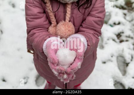 Little girl with pink coat and pink gloves holding snow outside in winter Stock Photo